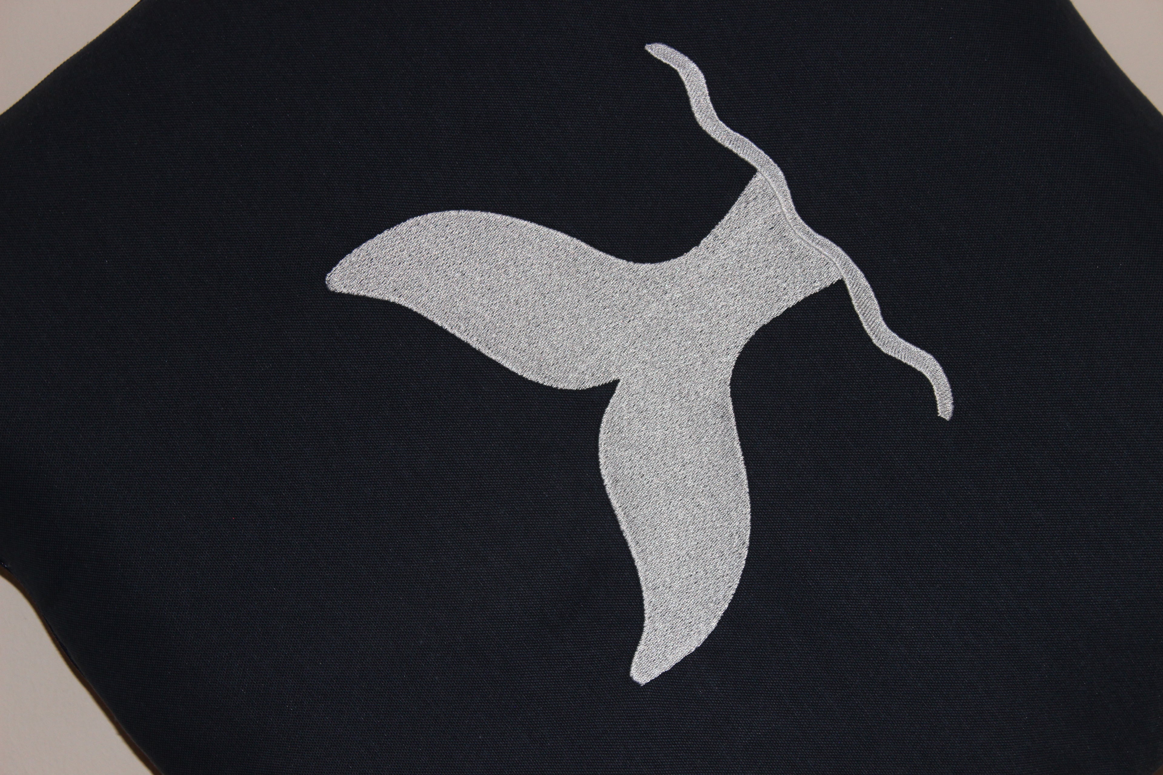 Close-up of white whale tail embroidery on navy blue convertible outdoor cushion by Mecks