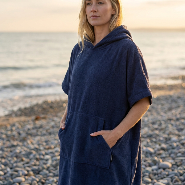 Woman wearing a navy blue hooded poncho on a pebbly beach.